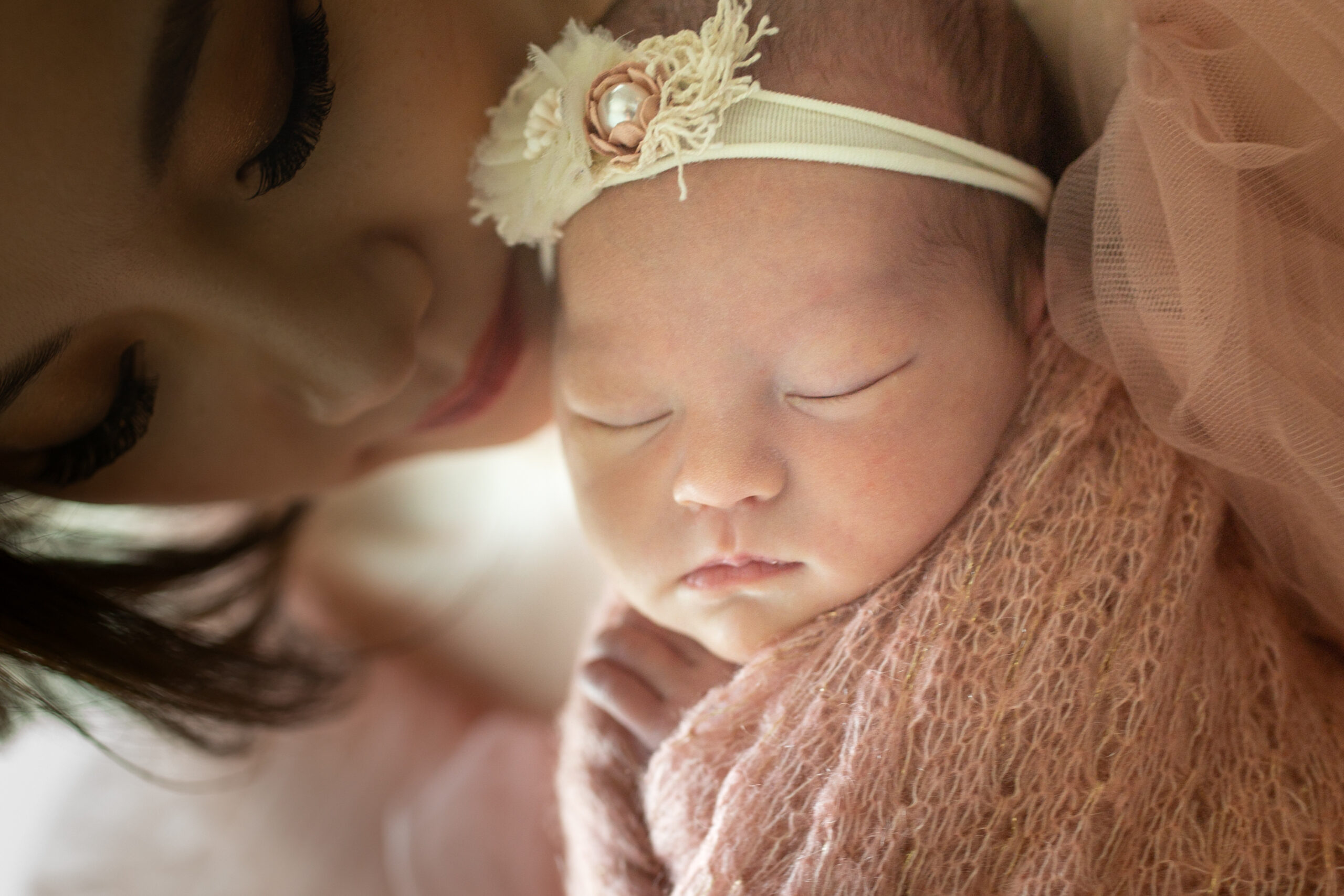 Tender moment between a mother and her newborn baby girl, both bathed in soft natural light; the baby wears a delicate headband and is peacefully cradled in her mother’s arms. Photographed in Los Angeles by Kendra Greenberg Photography.